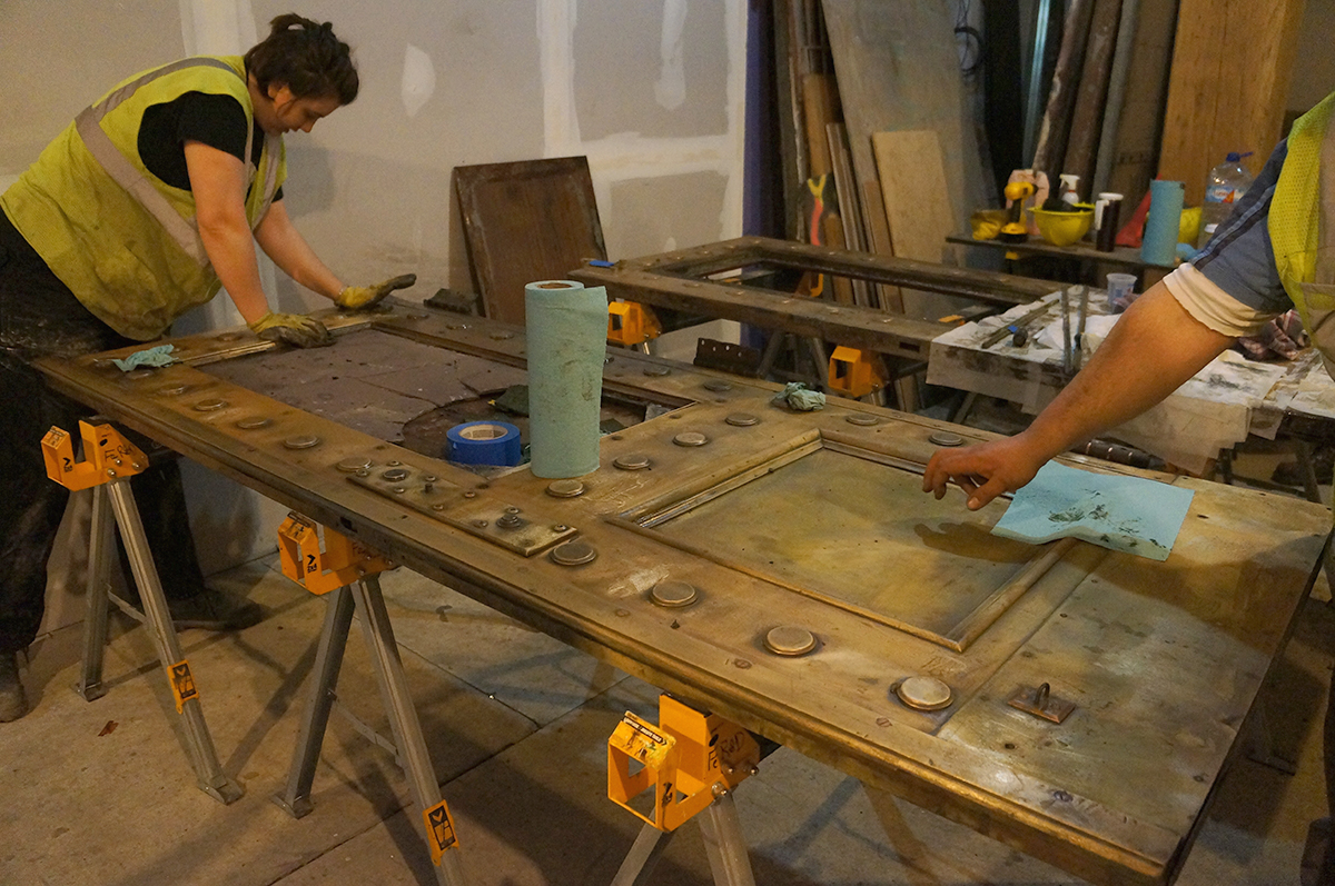 Restorers from Ferrous Research and Design polish a steel elevator door.